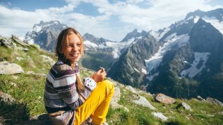 Jente på fjelltur, hun sitter på en stein og smiler
