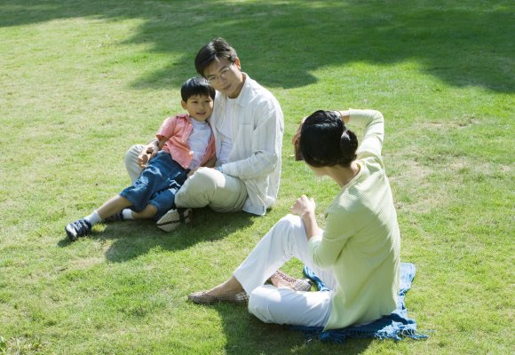 En asiatisk familie sitter på gresset i en park
