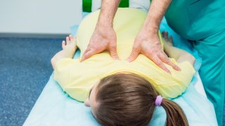 Fysioterapeut behandler ryggen til en kvinne som ligger på massasjebenk