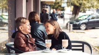 To barn på cafe ler og drikker sjokolademelk med sugerør