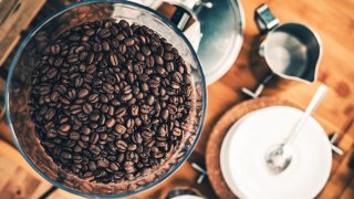 Kaffebønner i kaffekvern, fotografert ovenfra, med annet bryggeutstyr i bakgrunnen.