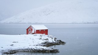 rødt naust ytterst på nes i en fjor, vinterbilde