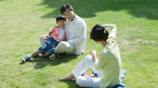 En asiatisk familie sitter på gresset i en park