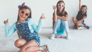 Tre jenter med solbriller sitter på skateboard og gjør peace-tegn med hendene