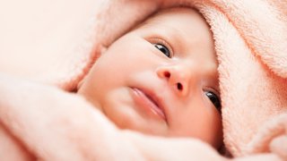 Nærbilde av ansiktet til en baby pakket inn i et mykt håndkle