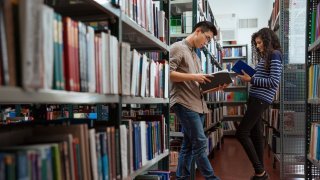 To voksne mennesker er i et bibliotek og leser. 