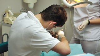 Tannlege som behandler en pasient mens en tannpleier står ved siden av.
