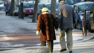Eldre par spaserer hånd i hånd på fortau