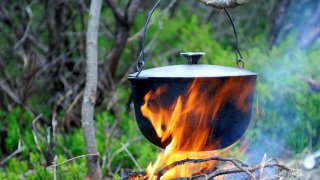 Gryte som koker på bål i naturen