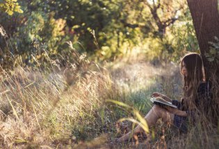 Jente som leser bok i skogen.