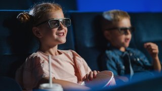 Barn sitter i kinosal med 3d-briller og spiser popkorn