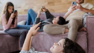 Familie sitter i stua og aller ser på mobiltelefonene sine