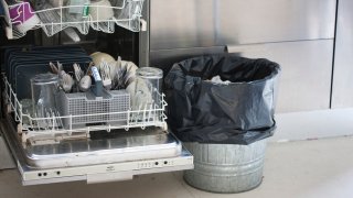 Oppvaskmaskin med møkkete oppvask og søppelbøtte ved siden av.