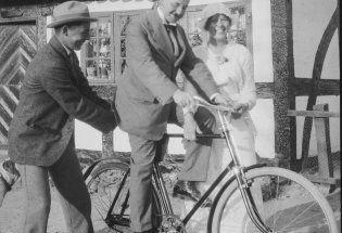 Historisk bilde av mann på sykkel sammen med dame og mann