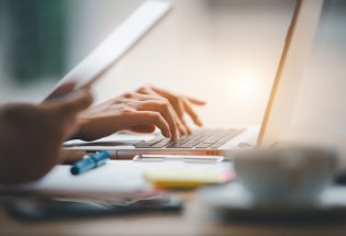 skriver på laptop, kaffekopp, papirer