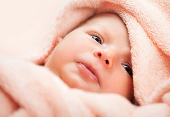 Nærbilde av ansiktet til en baby pakket inn i et mykt håndkle